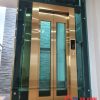 Thang máy vách kính gia đình inox sọc vàng xen inox kính xanh