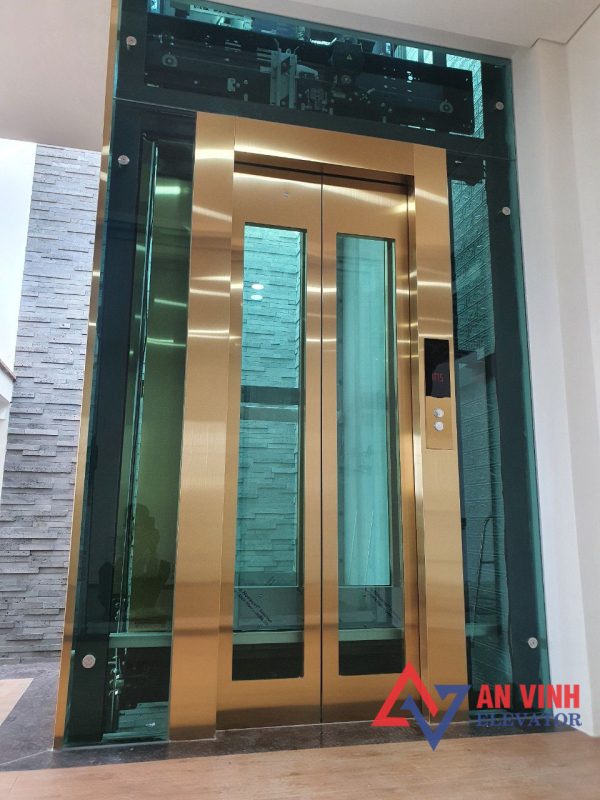 Thang máy vách kính gia đình inox sọc vàng xen inox kính xanh